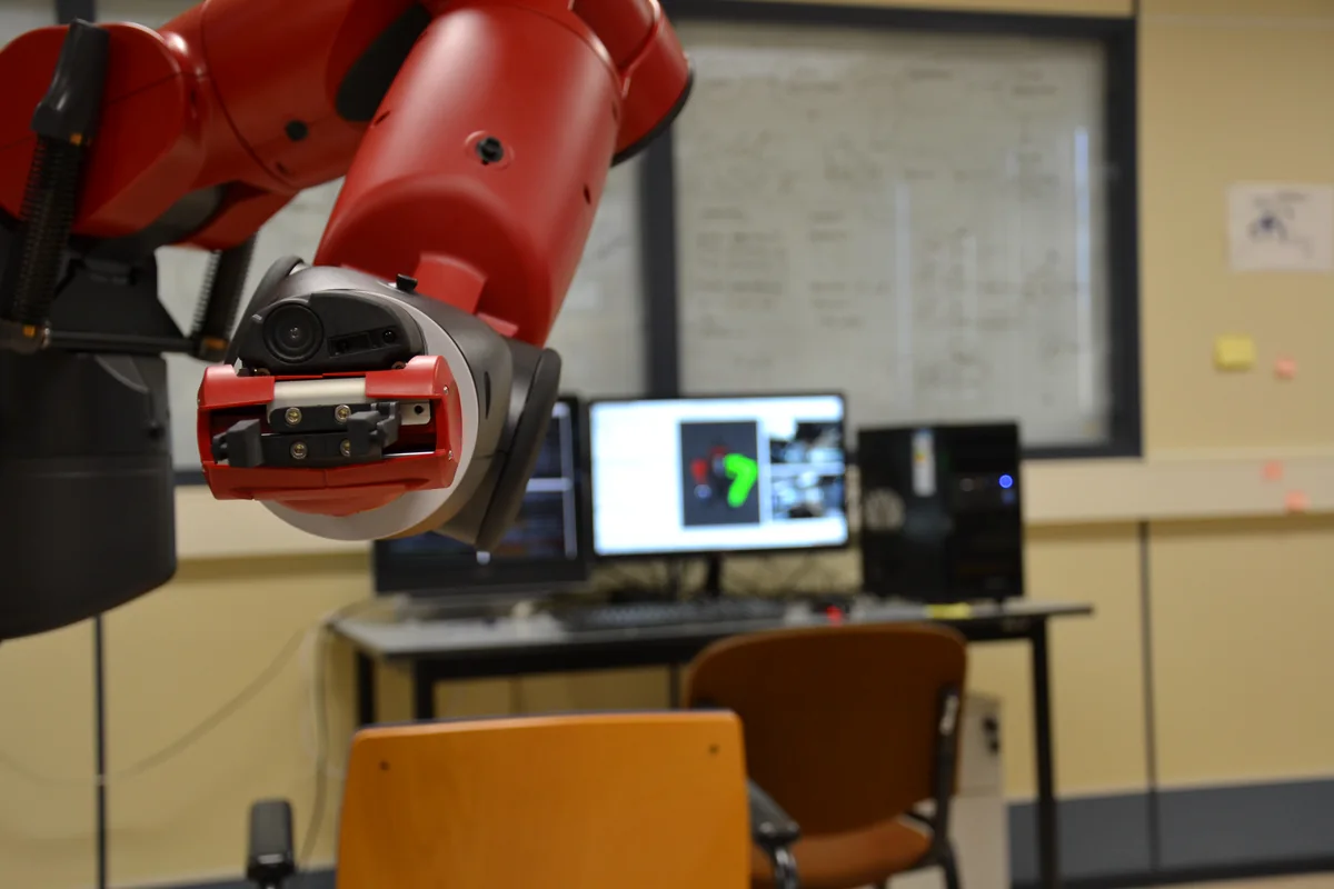 Close view of a red Baxter robot arm and its gripper in a robotics laboratory.